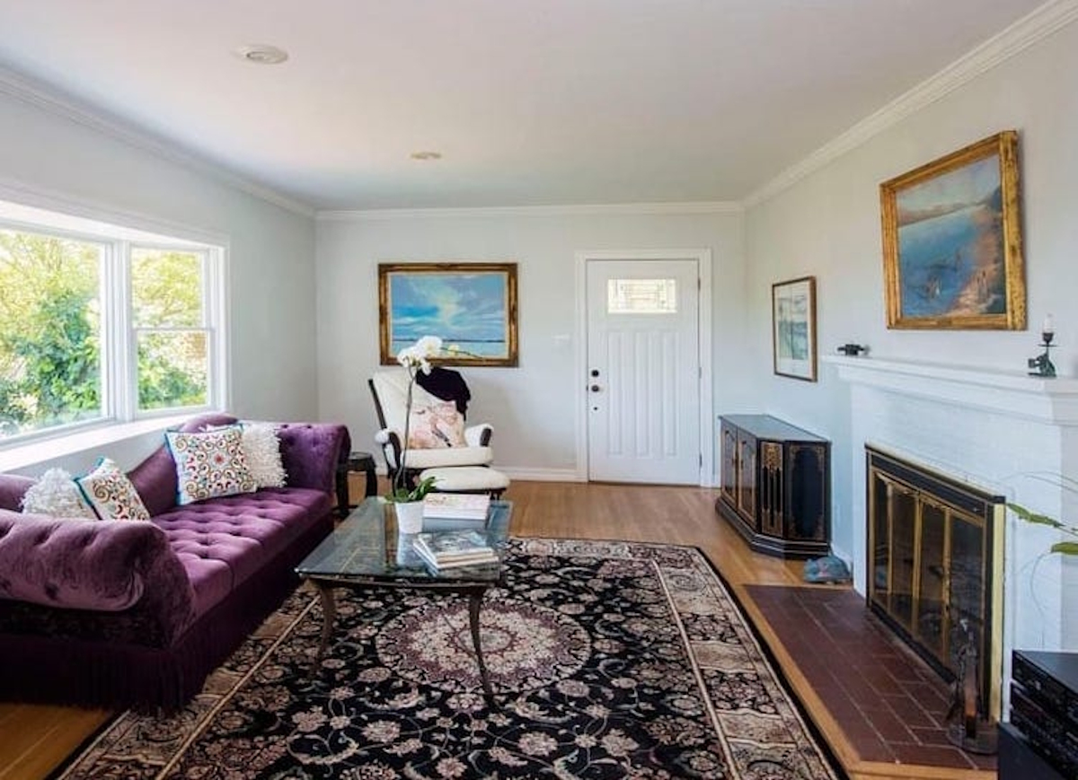 A living room with white paint, wooden floors, a purple couch, and a fireplace