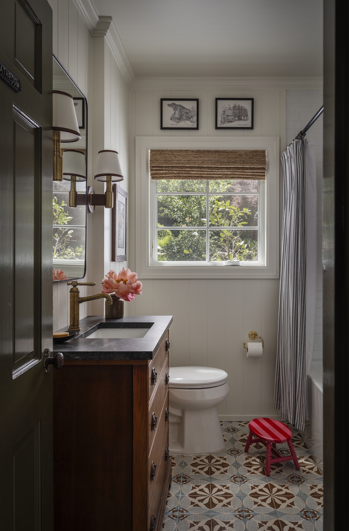 A bathroom with patterned tile, a wooden vanity, and artwork above the window